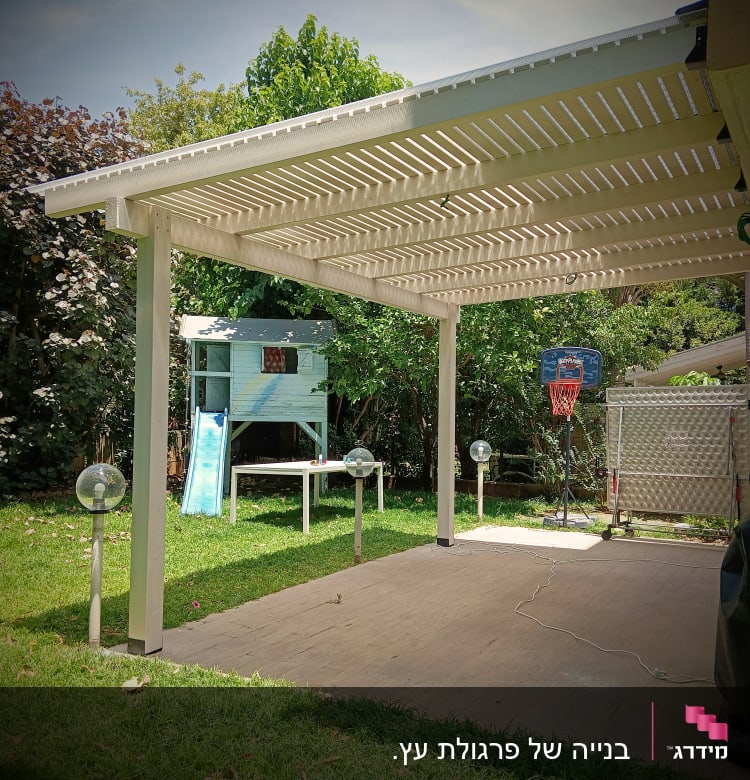 פרגולה לבנה בגינה עם דשא ירוק ומתקן כדורסל